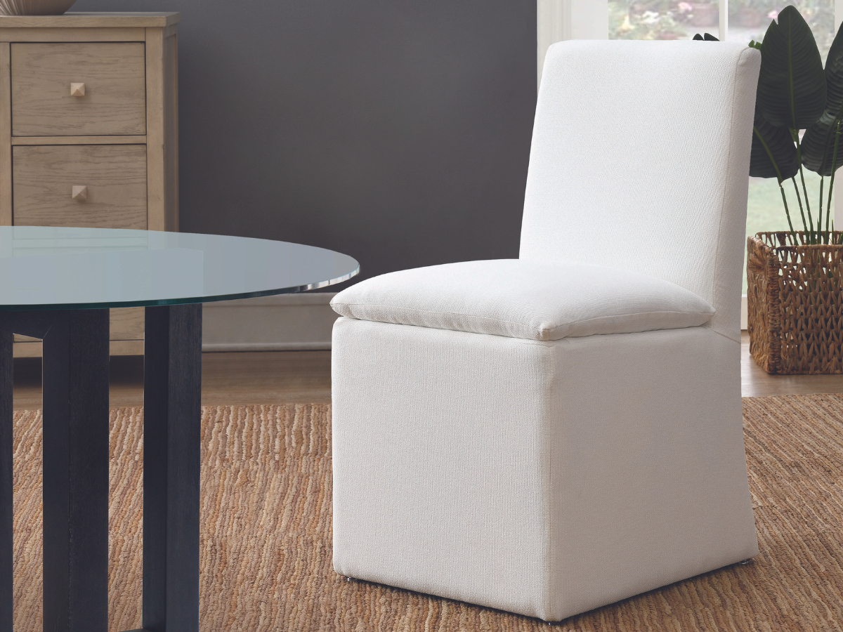 A white chair positioned in front of a sleek glass table, creating a modern and minimalist aesthetic.