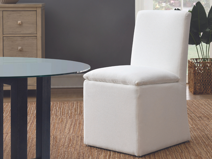 A white chair positioned in front of a sleek glass table, creating a modern and minimalist aesthetic.
