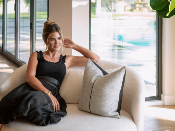 A woman seated on a couch in a cozy living room, surrounded by warm decor and soft lighting